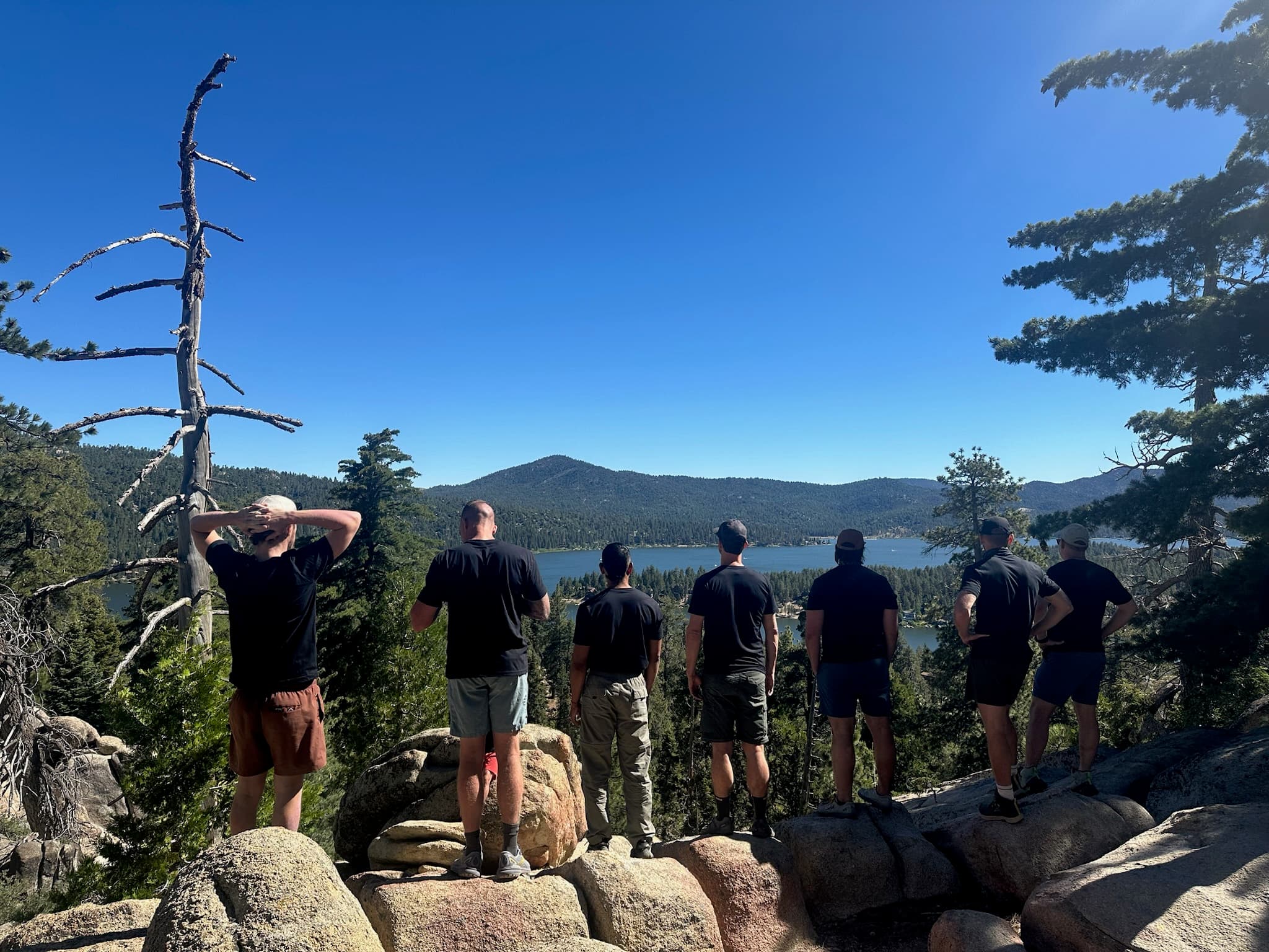 A group of individuals standing on rocks, gazing at a scenic lake and mountains